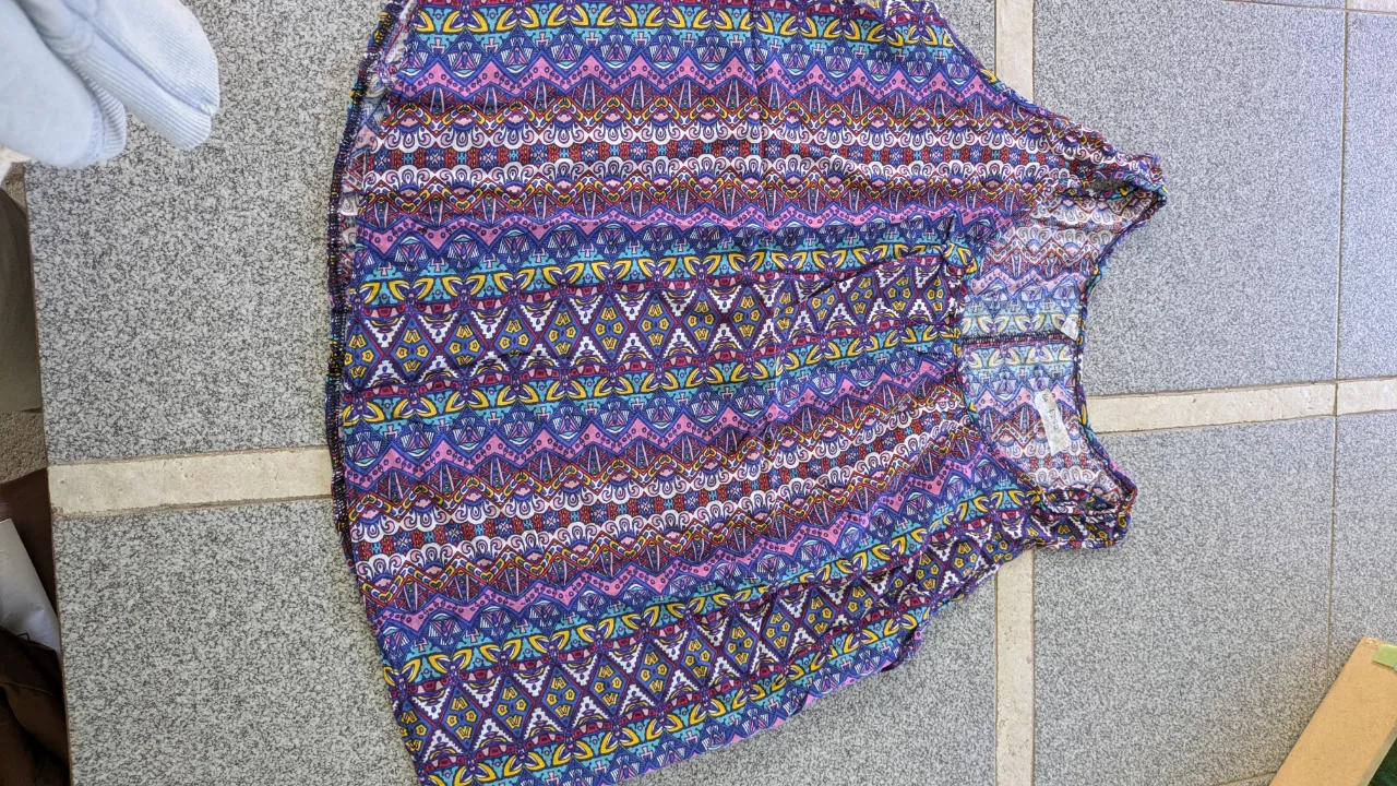 Remera estampada con motivos geométricos y tribales en colores vibrantes como fucsia, azul, amarillo y verde. Posee cuello redondo y mangas cortas.