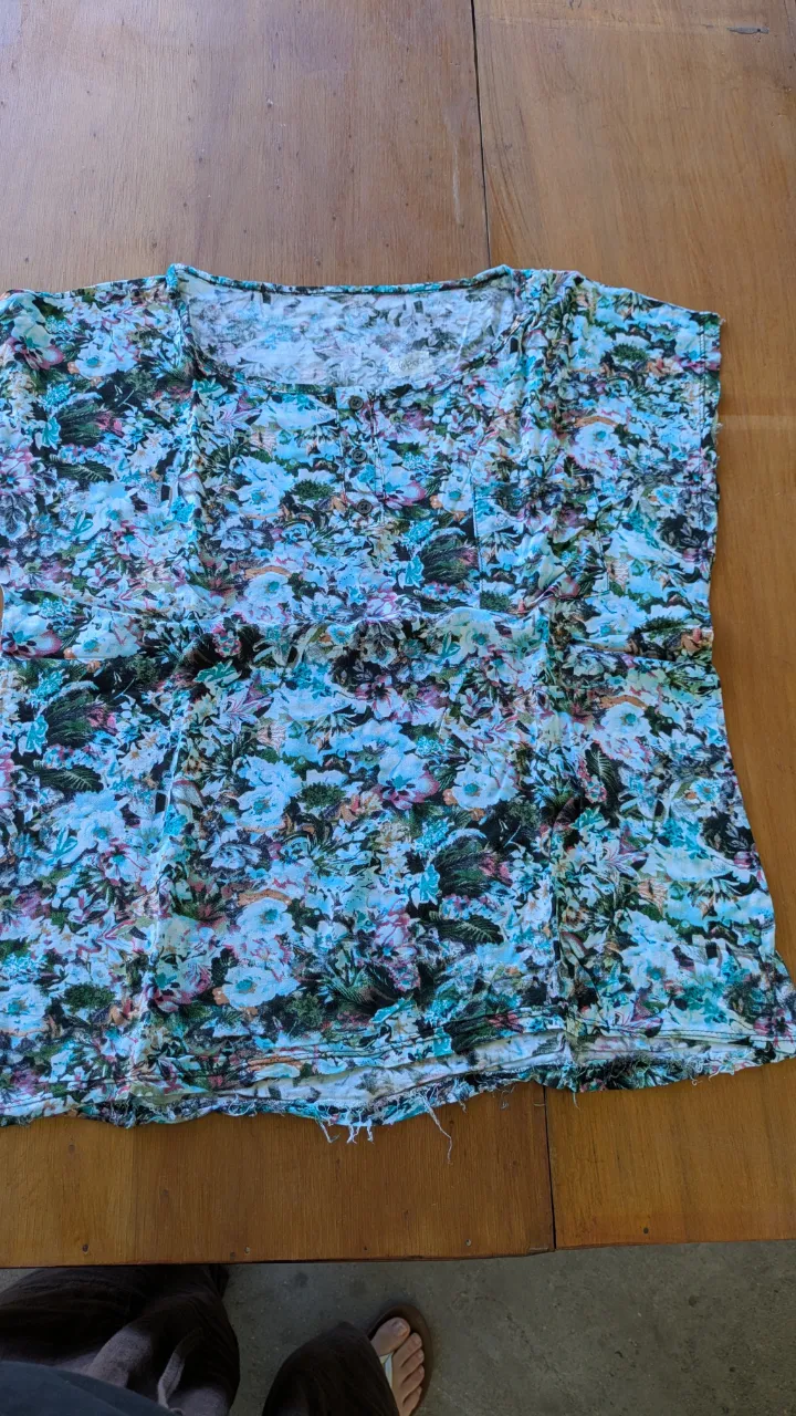 Remera estampada con flores y hojas en tonos celestes, verdes y rosas. Posee un escote redondo y tres botones en la parte superior delantera. Ideal para un look casual y fresco.