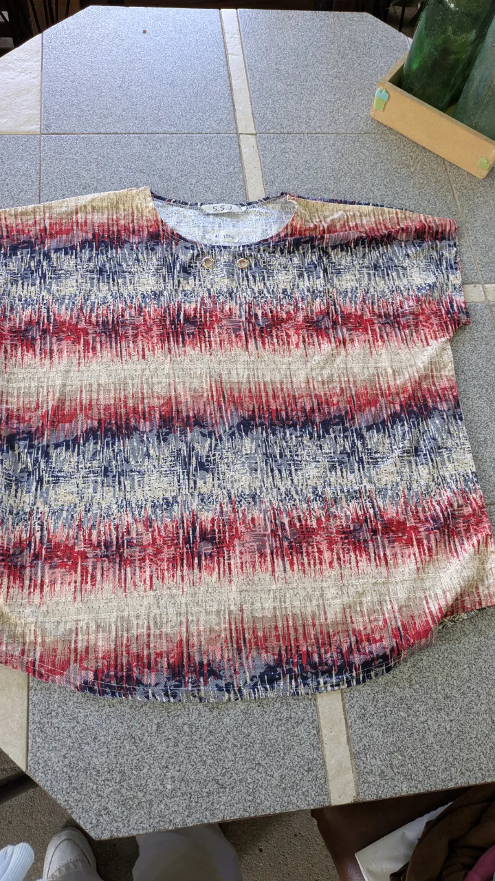 Remera estampada con rayas verticales y horizontales en tonos azules, rojos y beige. Posee dos ojales dorados en la parte superior delantera. talle M/L