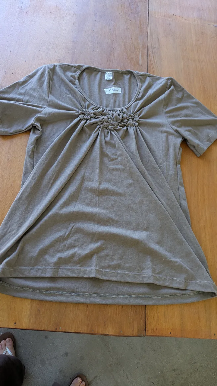 Remera manga corta de color marrón, con un detalle de fruncido y flores en el escote. Ideal para un look casual y cómodo.