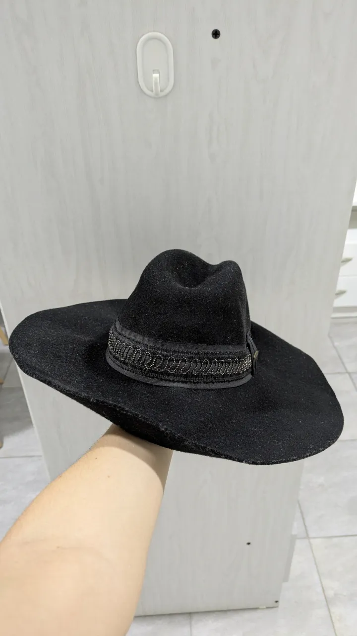 Sombrero negro de ala ancha con cinta decorada con bordado y detalle metálico con la marca. 