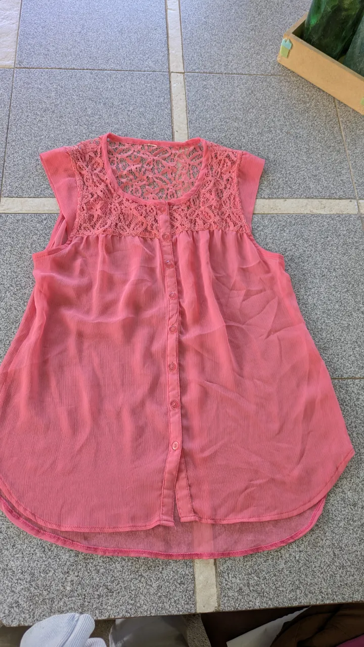 Blusa rosa sin mangas con cuello redondo y detalles de encaje en la parte superior. Posee botones al frente.