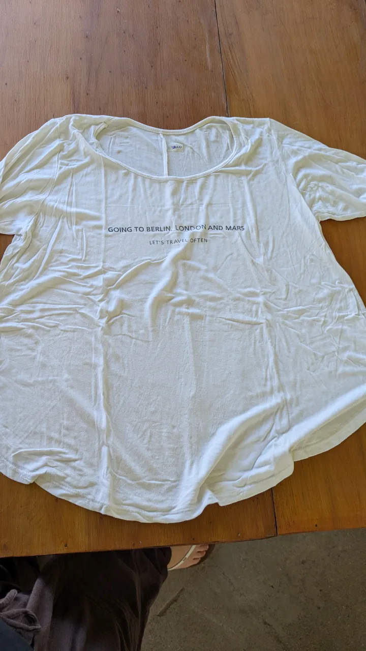 Remera blanca con estampa "GOING TO BERLIN, LONDON AND MARS LET'S TRAVEL OFTEN". Cuello redondo y mangas cortas. Ideal para un look casual y cómodo.