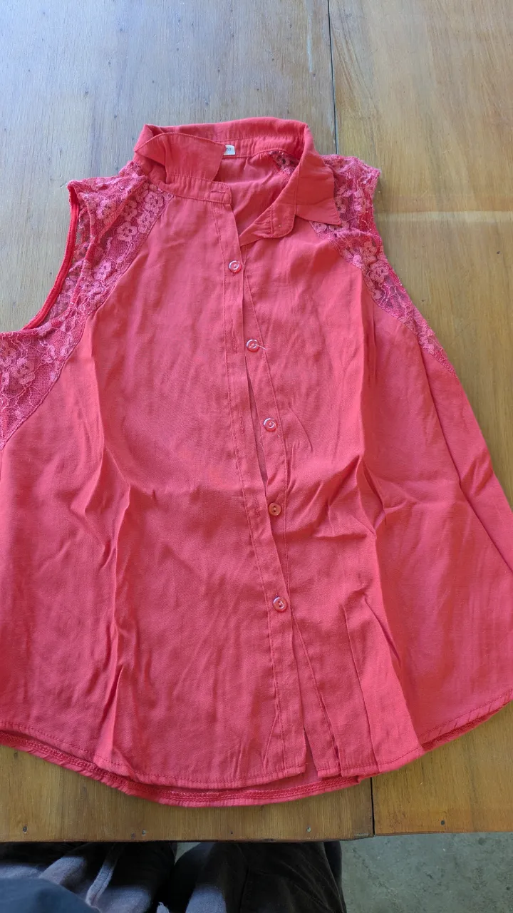 Remera coral con detalles de encaje en los hombros. Diseño sin mangas, con cuello de camisa y botones al frente. Ideal para un look fresco y femenino.