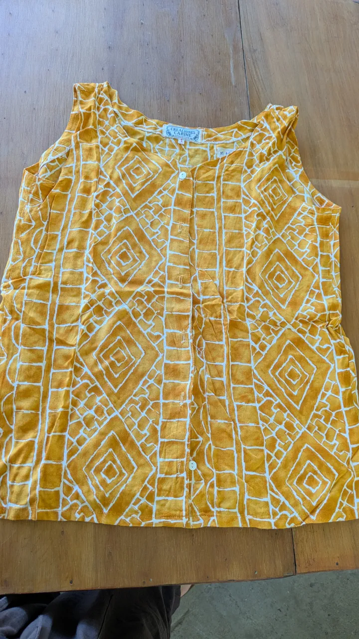 Remera estampada con un diseño geométrico en tonos amarillos y blancos. Posee botones en la parte delantera y es sin mangas, ideal para los días cálidos. talle 1 grande.