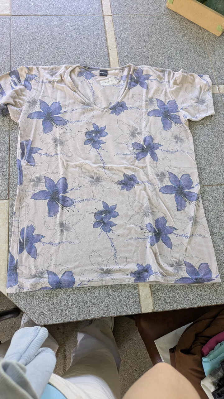 Remera de manga corta con cuello en V y estampa floral de flores grandes en tonos lilas y azules sobre fondo claro.