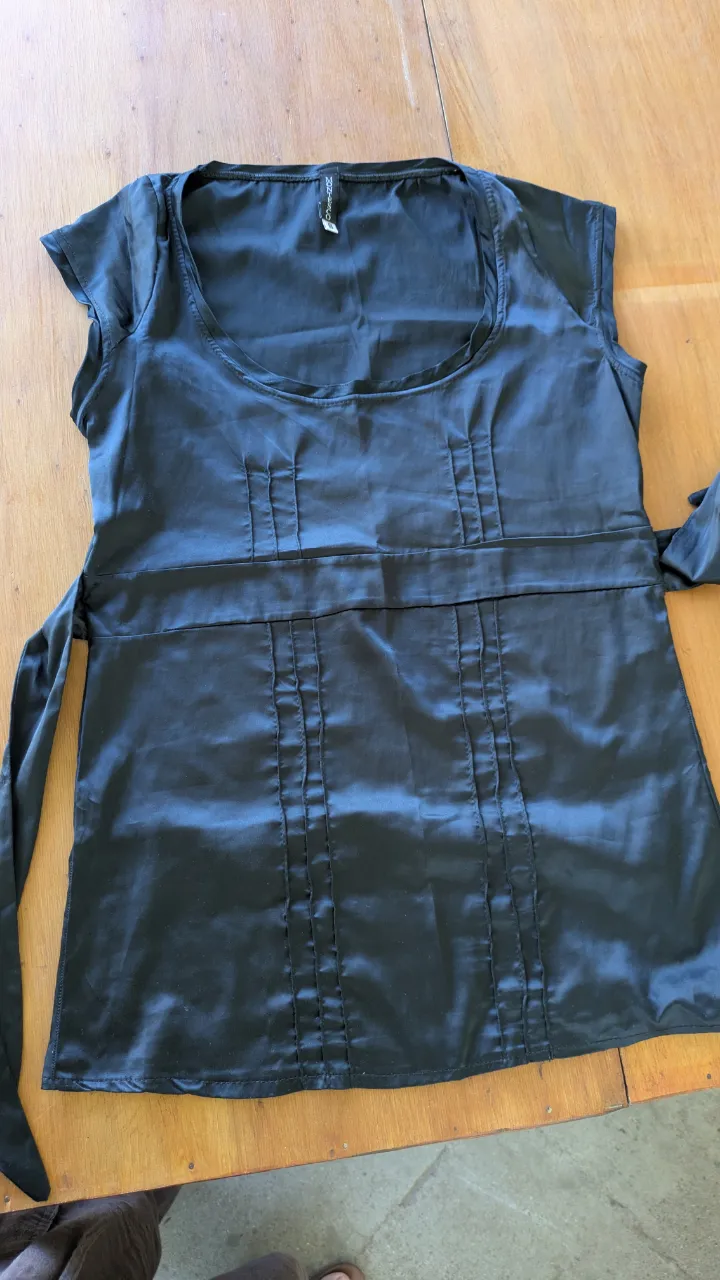 Remera negra de seda, con detalles de plisado en el frente y la espalda. Posee un lazo para atar en la cintura, que le da un toque delicado y femenino. Ideal para un look elegante y sofisticado.