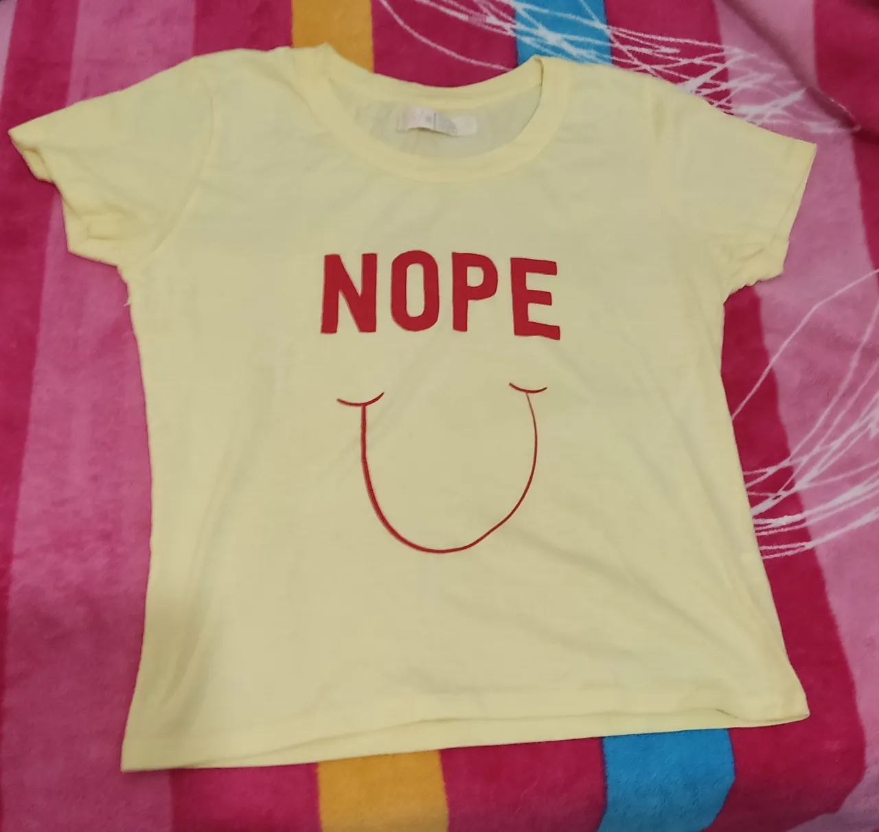 Remera de mujer de color amarillo claro con estampado "NOPE" en rojo y un diseño de sonrisa. Ideal para un look casual y divertido.