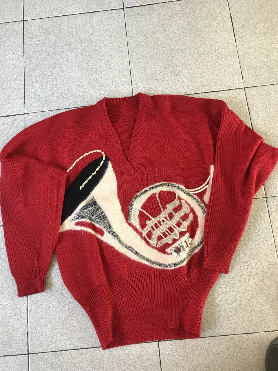 Sweater rojo con diseño de instrumento musical en relieve y detalles brillantes. Cuello en V y puños tejidos.