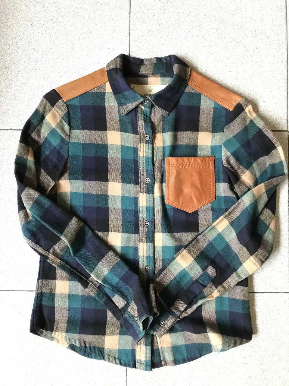 Camisa a cuadros de hombre, con detalles en cuero en los hombros y bolsillo. Estilo leñador, ideal para un look casual y canchero.