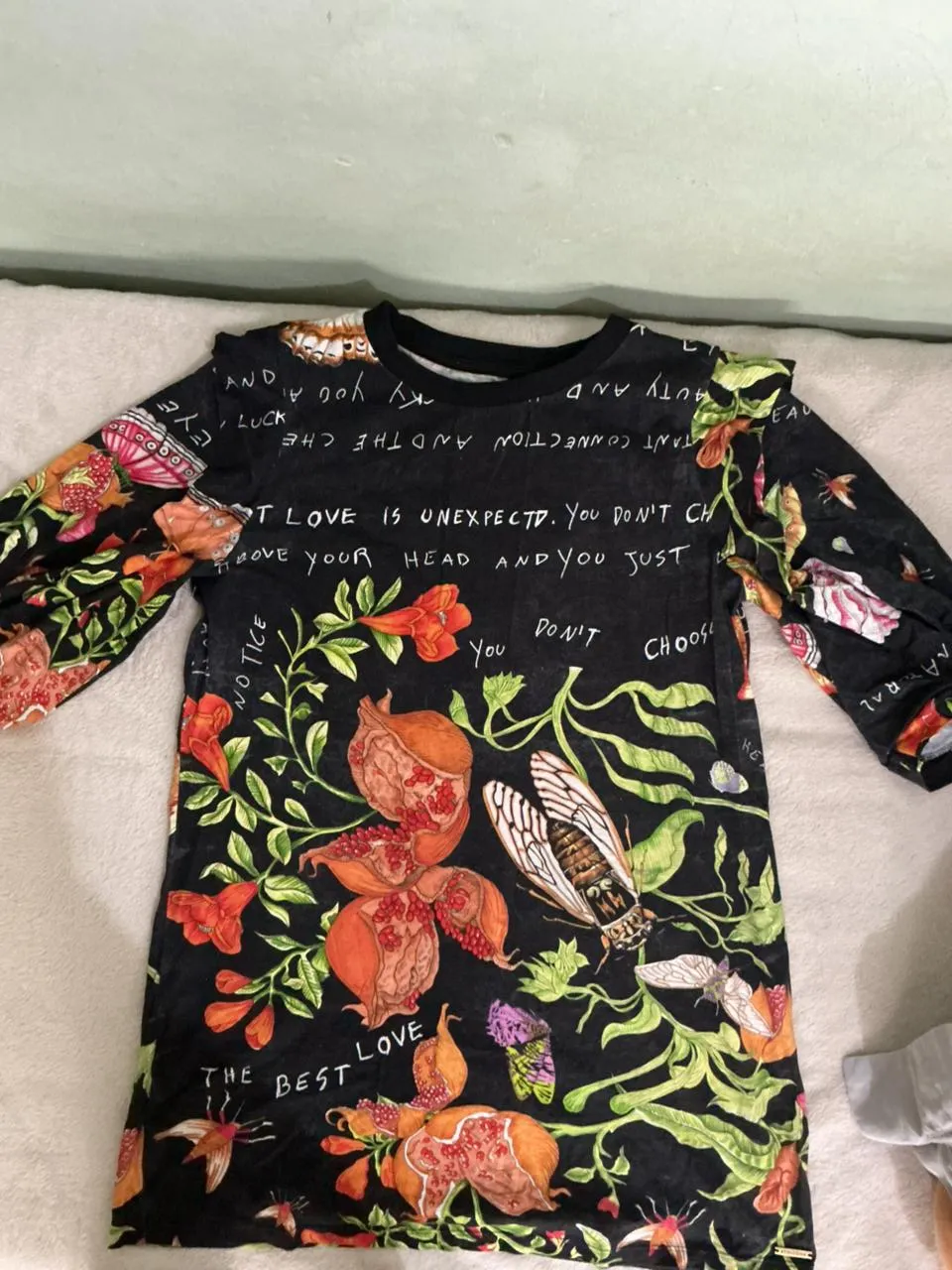 Remera negra con estampa de flores, insectos y frases. Posee mangas largas y cuello redondo. Ideal para un look casual y original.