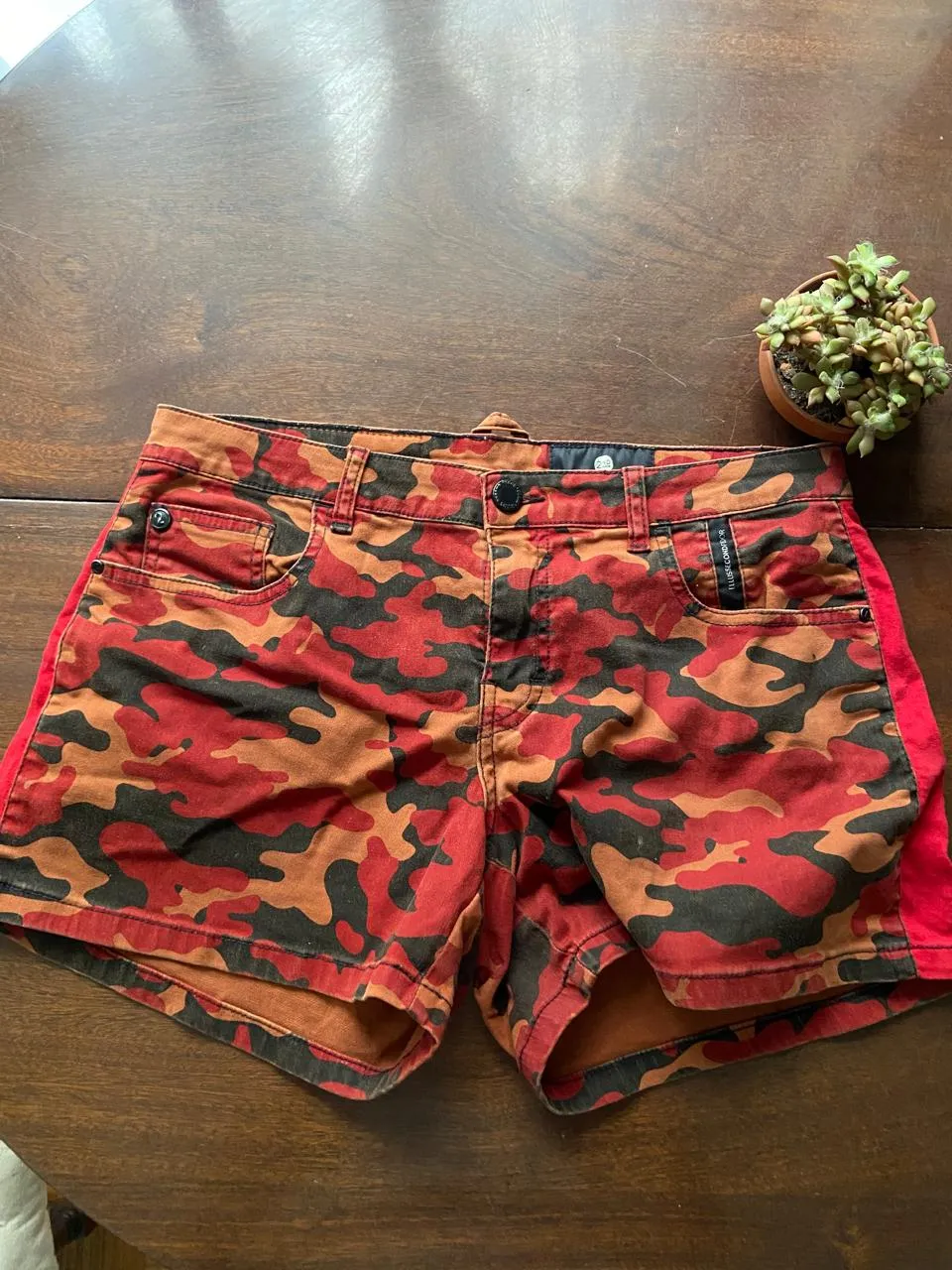 Shorts de jean con estampa camuflada en tonos rojos, naranjas y negros. Detalle de paneles laterales en color rojo liso. Ideales para un look urbano y canchero.