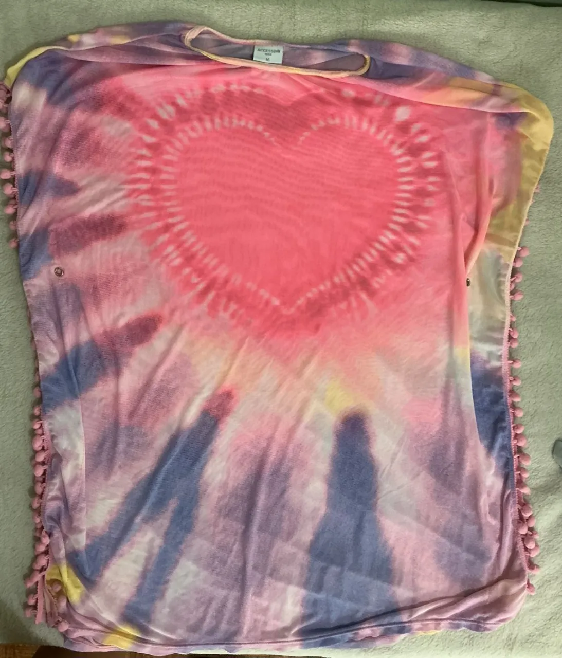 ¡Prenda súper canchera y colorida! Ideal para darle un toque divertido a tu look. Con un diseño tie-dye vibrante y un corazón central que enamora, tiene detalles de pompones en los bordes que le dan un toque único. Perfecta para sentirte cómoda y a la moda.