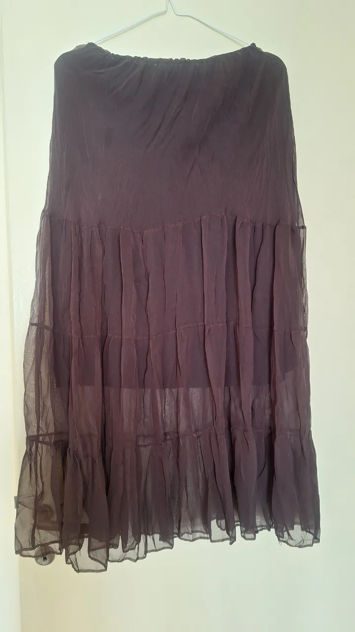 Pollera larga de gasa plisada en color marrón oscuro, con volados y detalles de diseño. Ideal para un look elegante y con movimiento.