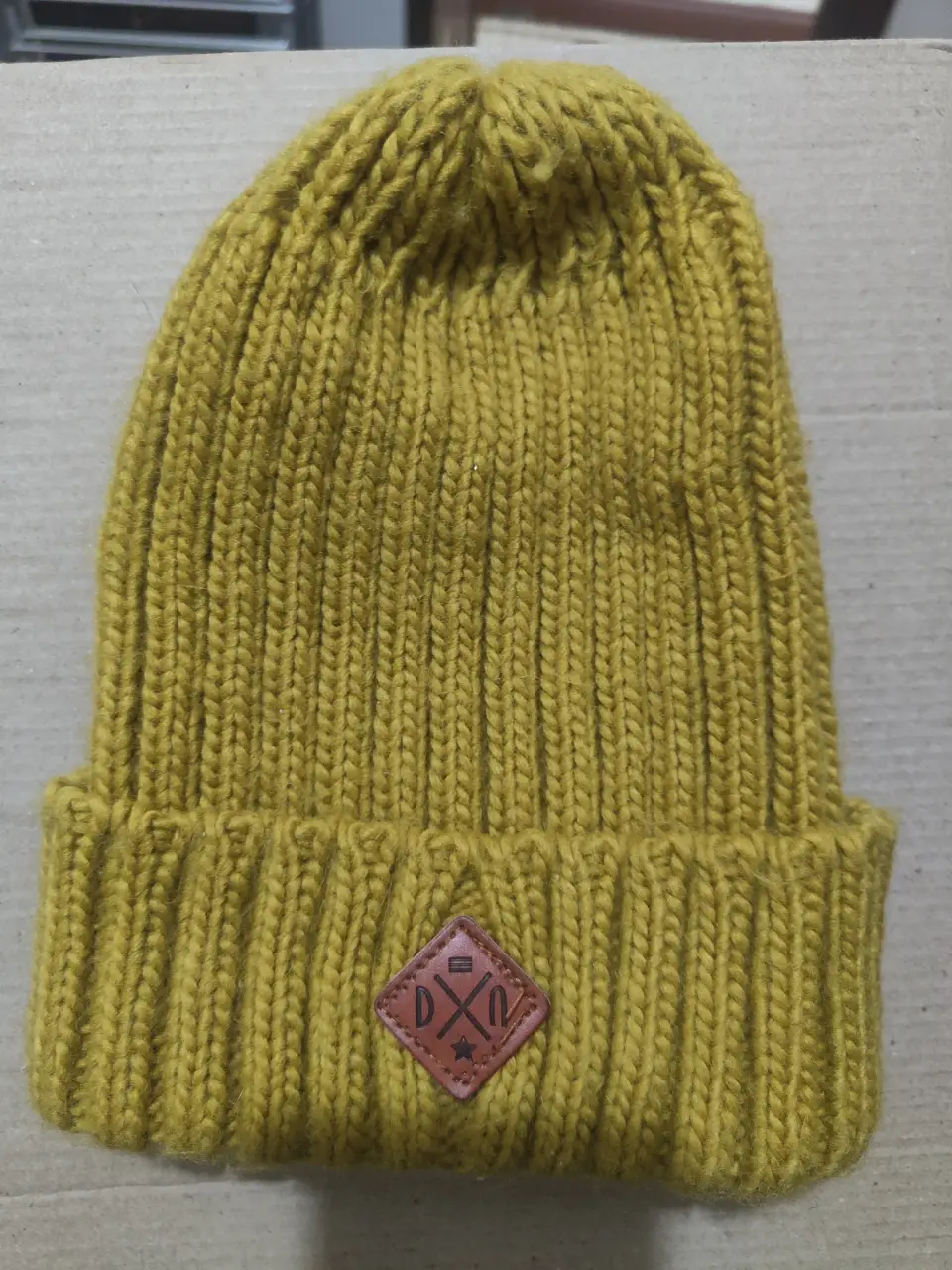 Gorro tejido de lana color mostaza con detalle de etiqueta de cuero con logo. Ideal para el invierno.