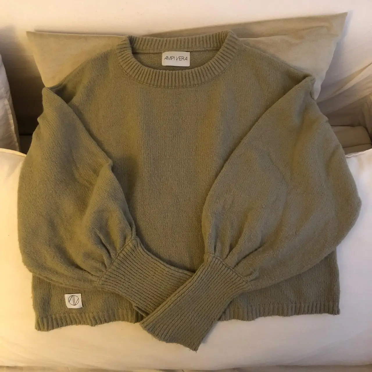 Sweater de mujer color crudo con mangas abullonadas y puños tejidos. Cuello redondo y etiqueta de la marca AMPIVERA.