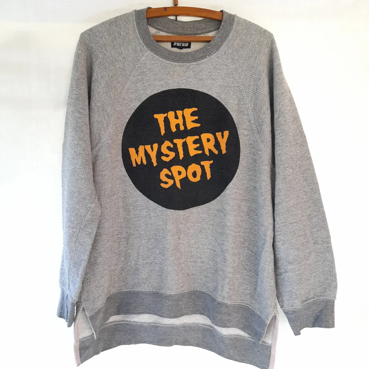 Buzo de cuello redondo gris con estampado "THE MYSTERY SPOT" en naranja y negro. Ideal para un look casual y urbano. Marca Ay not dead. Abrigado. Unisex.