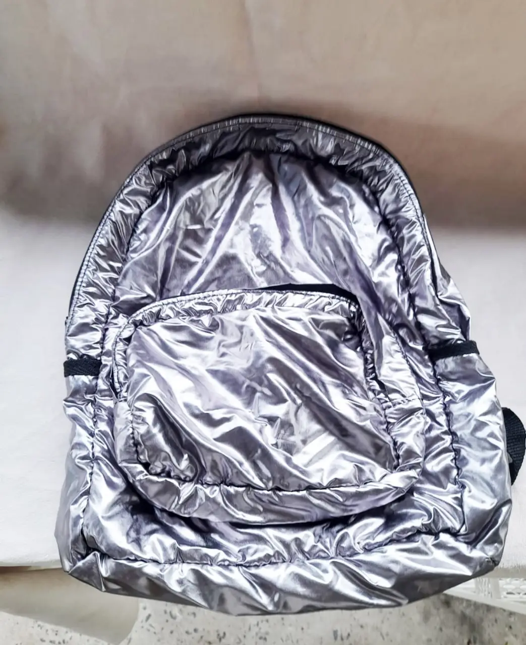 Mochila pequeña plateada con bolsillo frontal. Ideal para llevar tus cosas con estilo. Perfecta para el día a día. Marca complot. Como nueva.