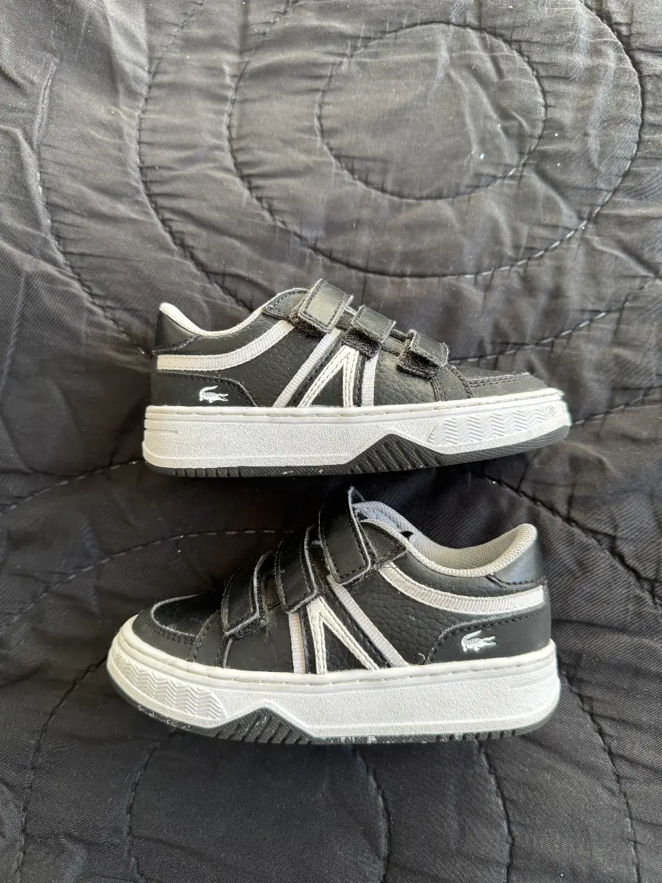 Zapatillas Lacoste para niños, negras con detalles en blanco y el logo del cocodrilo. Ideales para un look casual y cómodo.