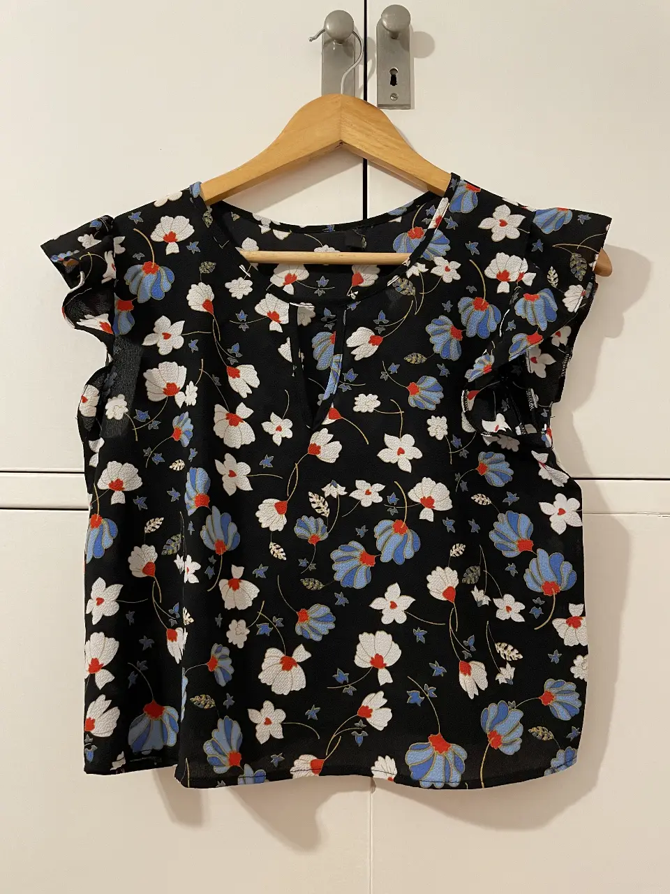Blusa de mujer con estampado floral en tonos blanco, azul y rojo sobre fondo negro. Diseño con mangas cortas con volados. Ideal para un look casual y fresco.