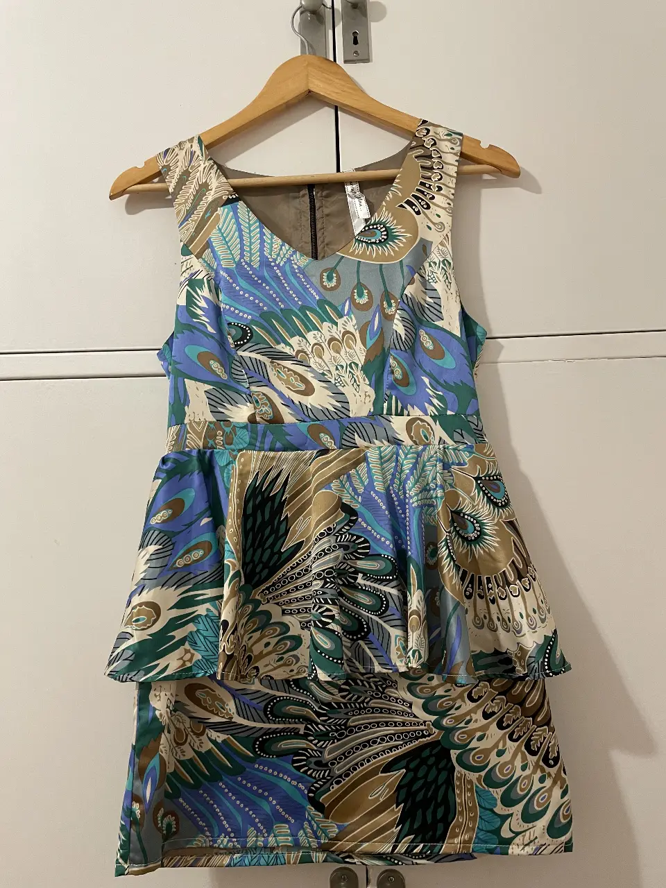 Vestido midi con estampado de plumas en tonos verdes, azules y marrones. Diseño con peplum en la cintura y cierre en la espalda.
