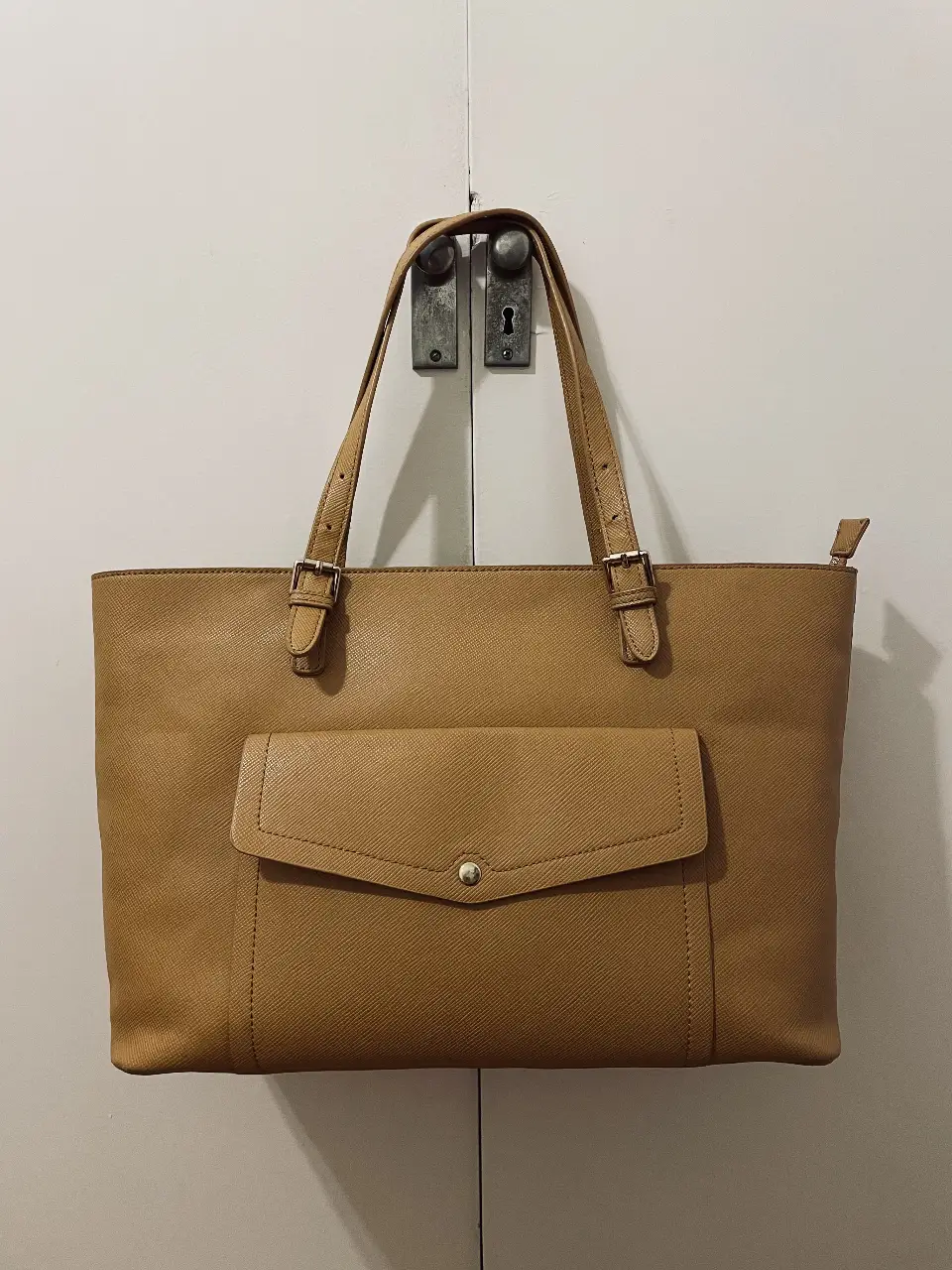 Cartera grande de cuero sintético color marrón claro. Posee un bolsillo frontal con botón a presión y cierre superior. Interior forrado en color naranja. Ideal para el trabajo o uso diario.
