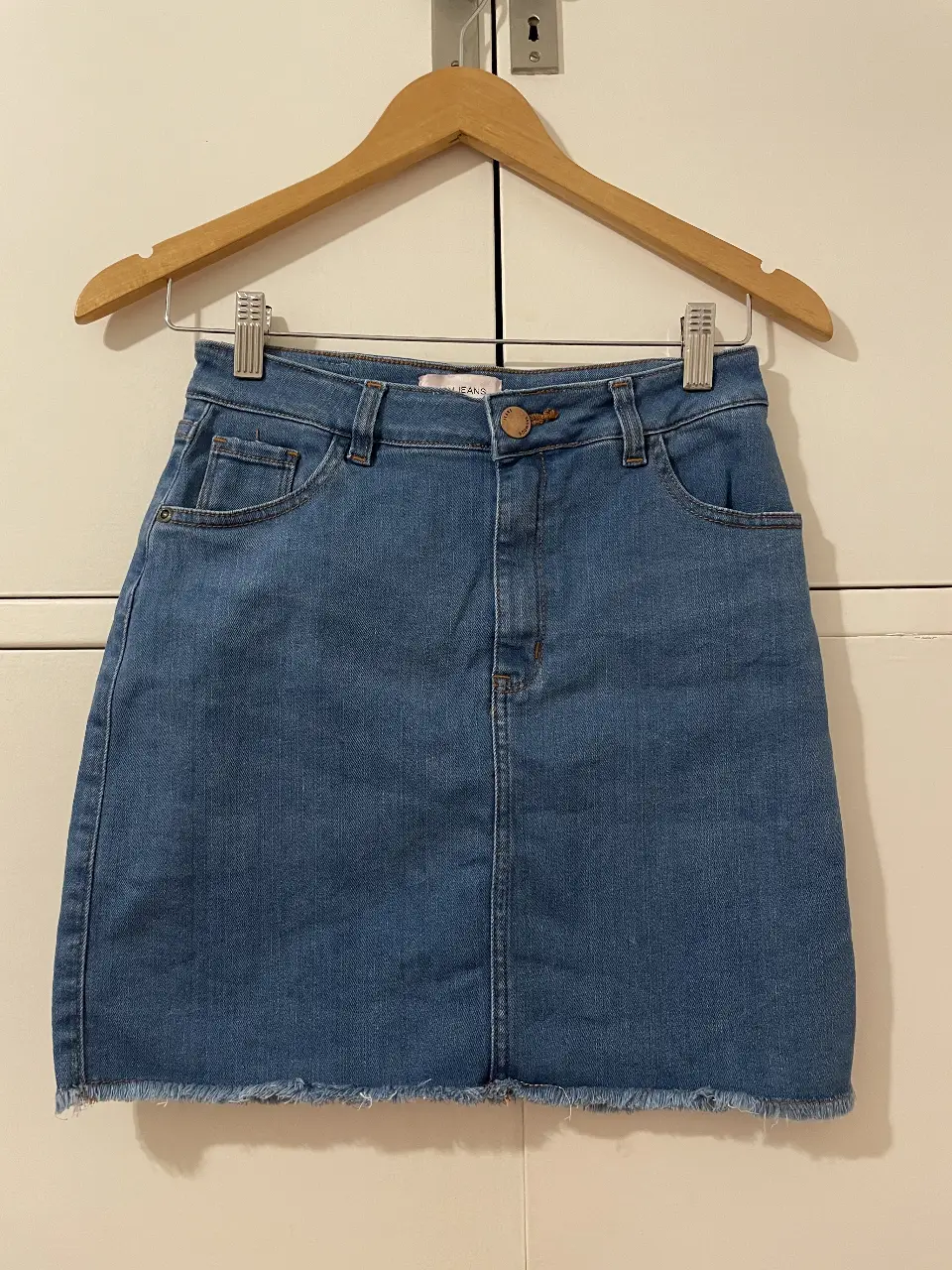 Pollera de jean azul, con un corte recto y un dobladillo deshilachado. Ideal para un look casual y moderno.