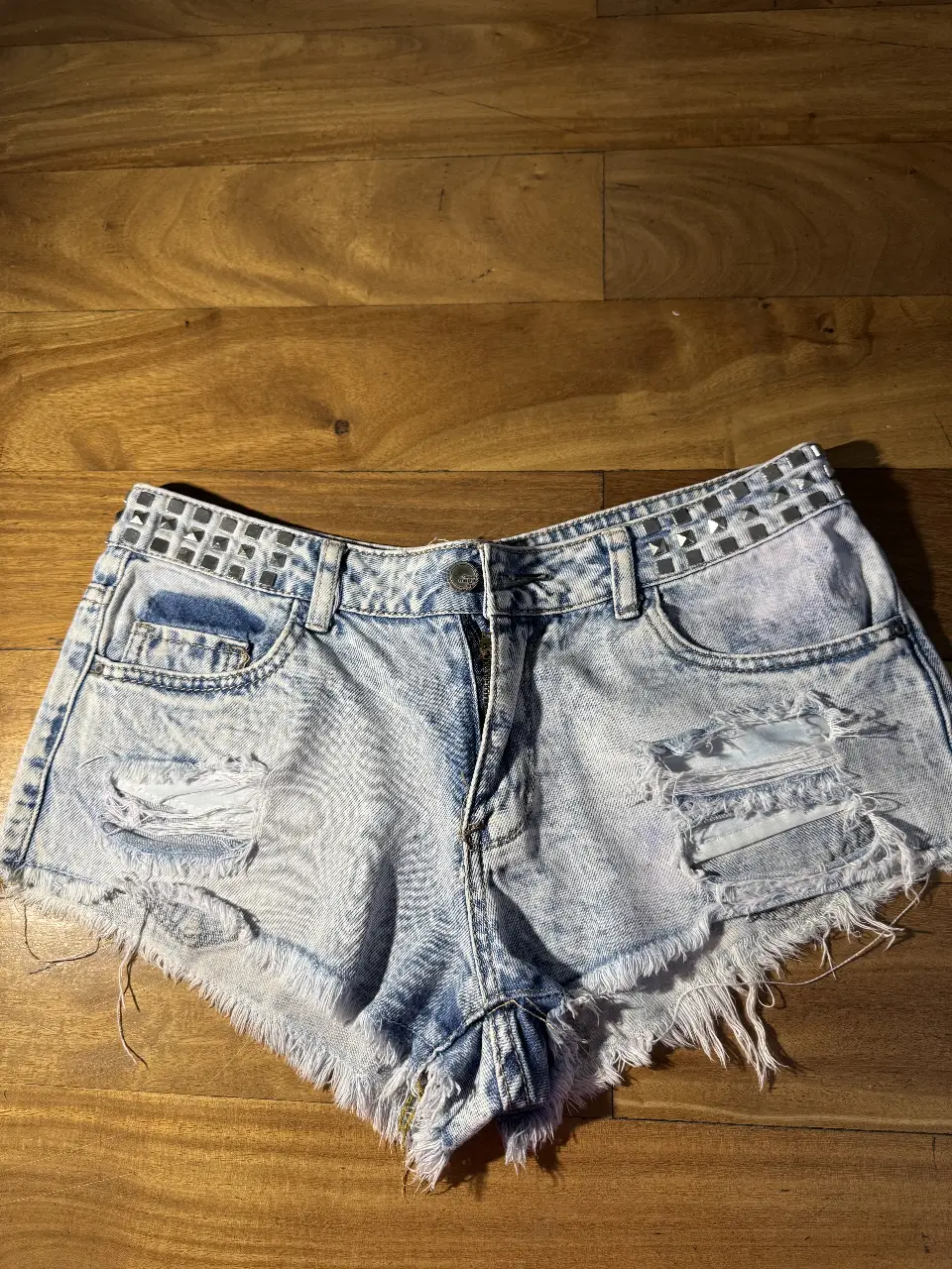Short de jean de mujer, tiro medio, con detalles rotos y tachas en los bolsillos. Ideal para un look casual y moderno.