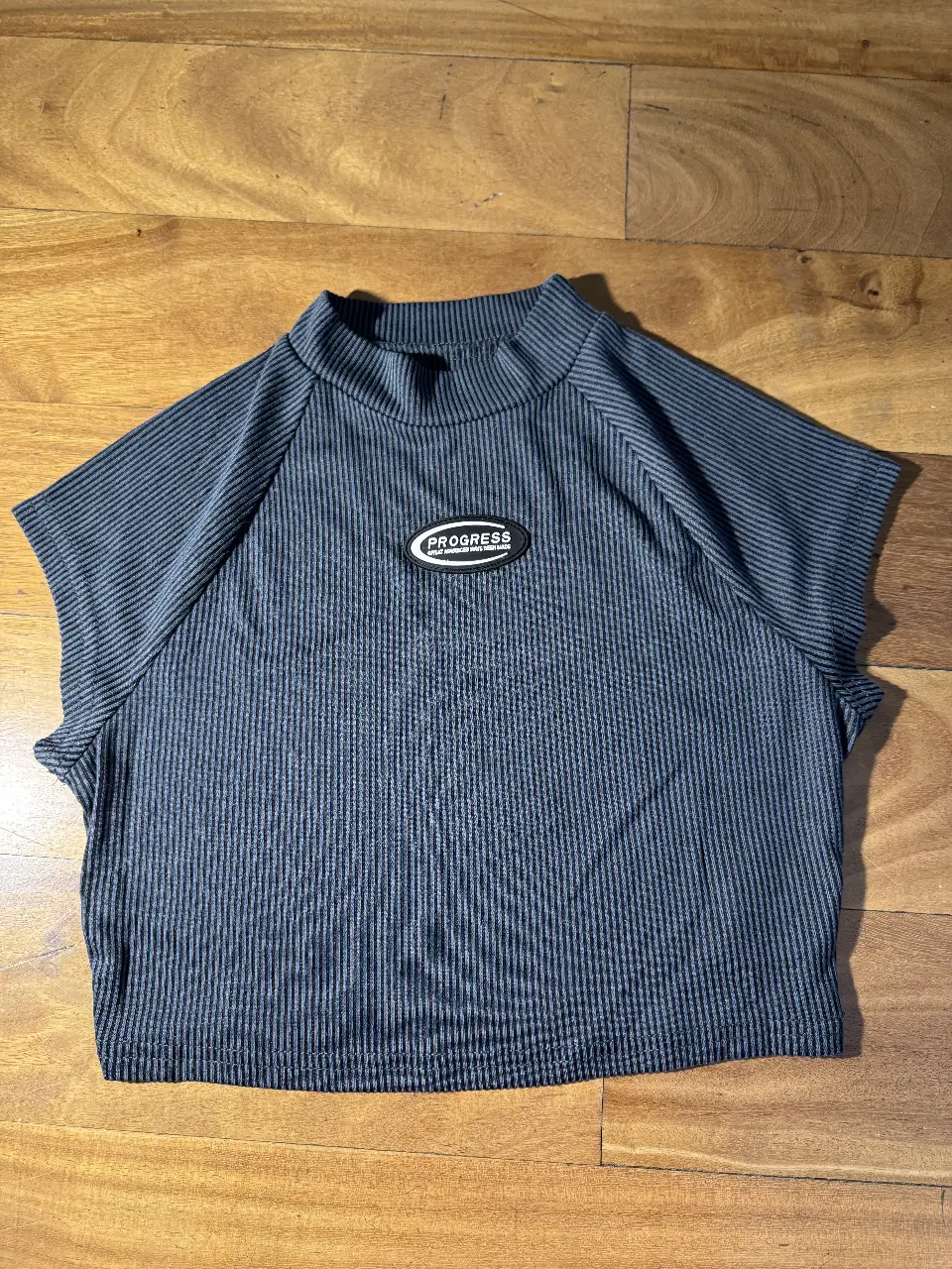 Top de cuello alto con detalle de etiqueta "PROGRESS" en el frente. Diseño con textura acanalada y corte crop, ideal para un look moderno y versátil.