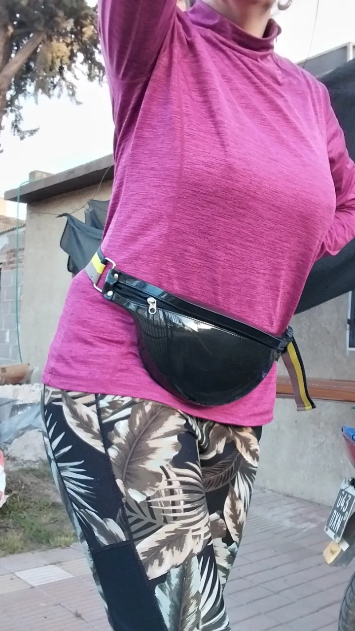 Riñonera negra de charol, con correa ajustable y detalles en amarillo y beige. Ideal para llevar lo esencial con estilo y comodidad.