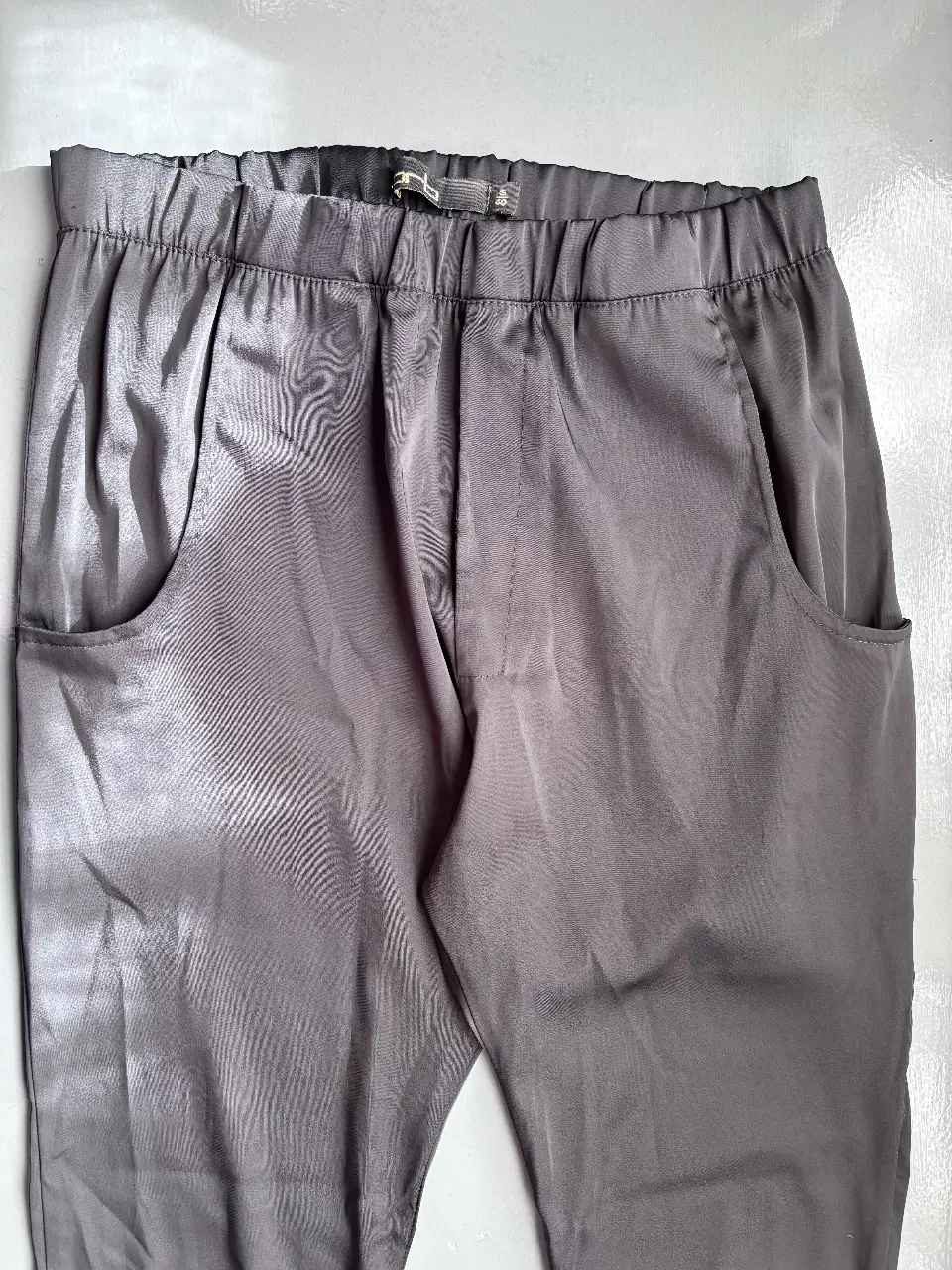 Pantalón sastrero de satén gris con bolsillos y cierre en el tobillo. Ideal para un look elegante y moderno.