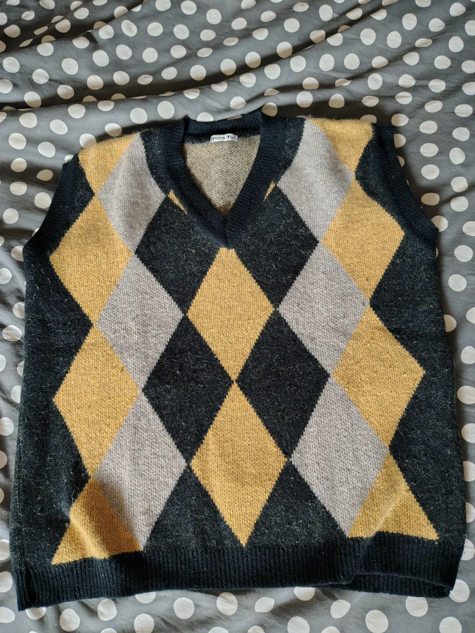 Chaleco de tejido de punto con rombos en negro, amarillo y gris. Cuello en V.