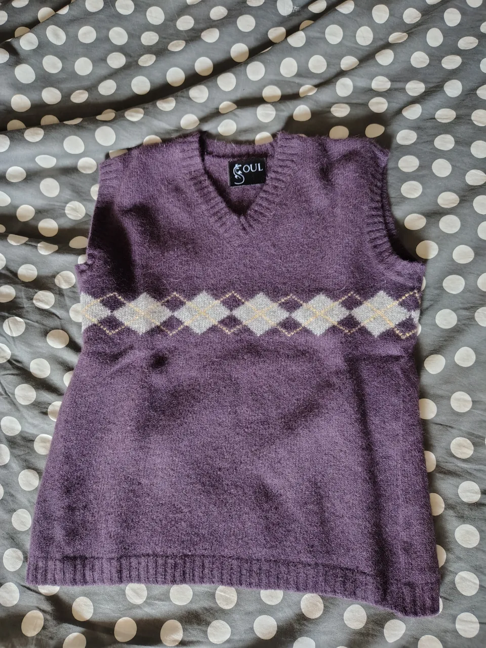 Sweater de lana sin mangas, color violeta, con cuello en V y un diseño de rombos en el pecho en tonos blanco y gris.