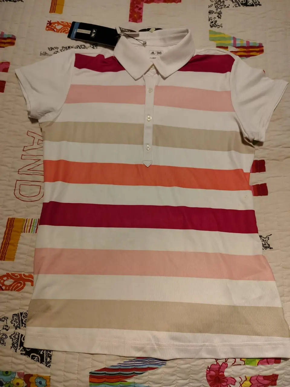 Remera Adidas ClimaCool de mujer, con diseño a rayas horizontales en tonos rosa, naranja y beige. Cuello polo y manga corta. Ideal para actividades deportivas o uso casual. Con etiqueta