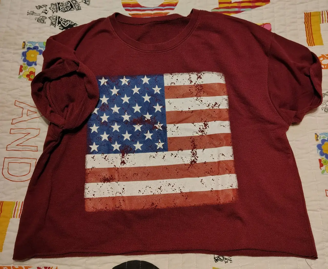 Remera manga corta de color bordó con estampado de la bandera de Estados Unidos desgastada. Corte recto y cuello redondo. Ideal para un look casual y patriótico.