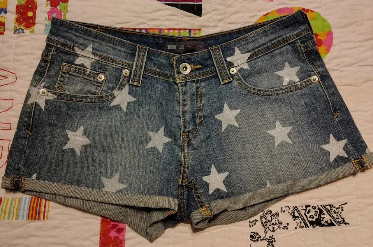 Short de jean de mujer, tiro medio, con estrellas blancas estampadas. Talle 26. Ideal para un look casual y canchero.