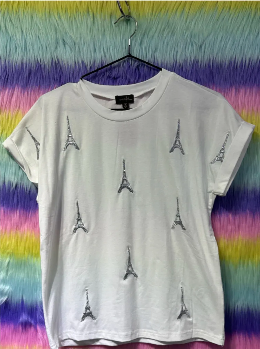 Remera blanca de mujer con estampado de la Torre Eiffel en lentejuelas. Corte clásico, manga corta con dobladillo. Ideal para un look casual y chic.