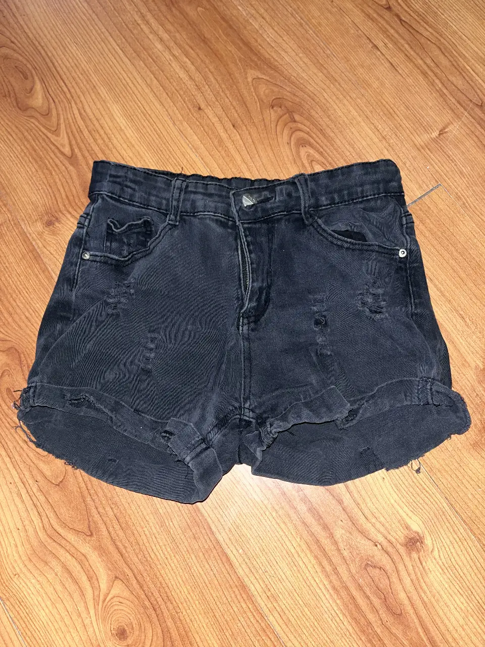 Short de jean negro gastado, con efecto vintage, roturas y ruedo desflecado. Tiro medio, calce cómodo y corte urbano. Talle 38/40 – va bien para talle S o M.