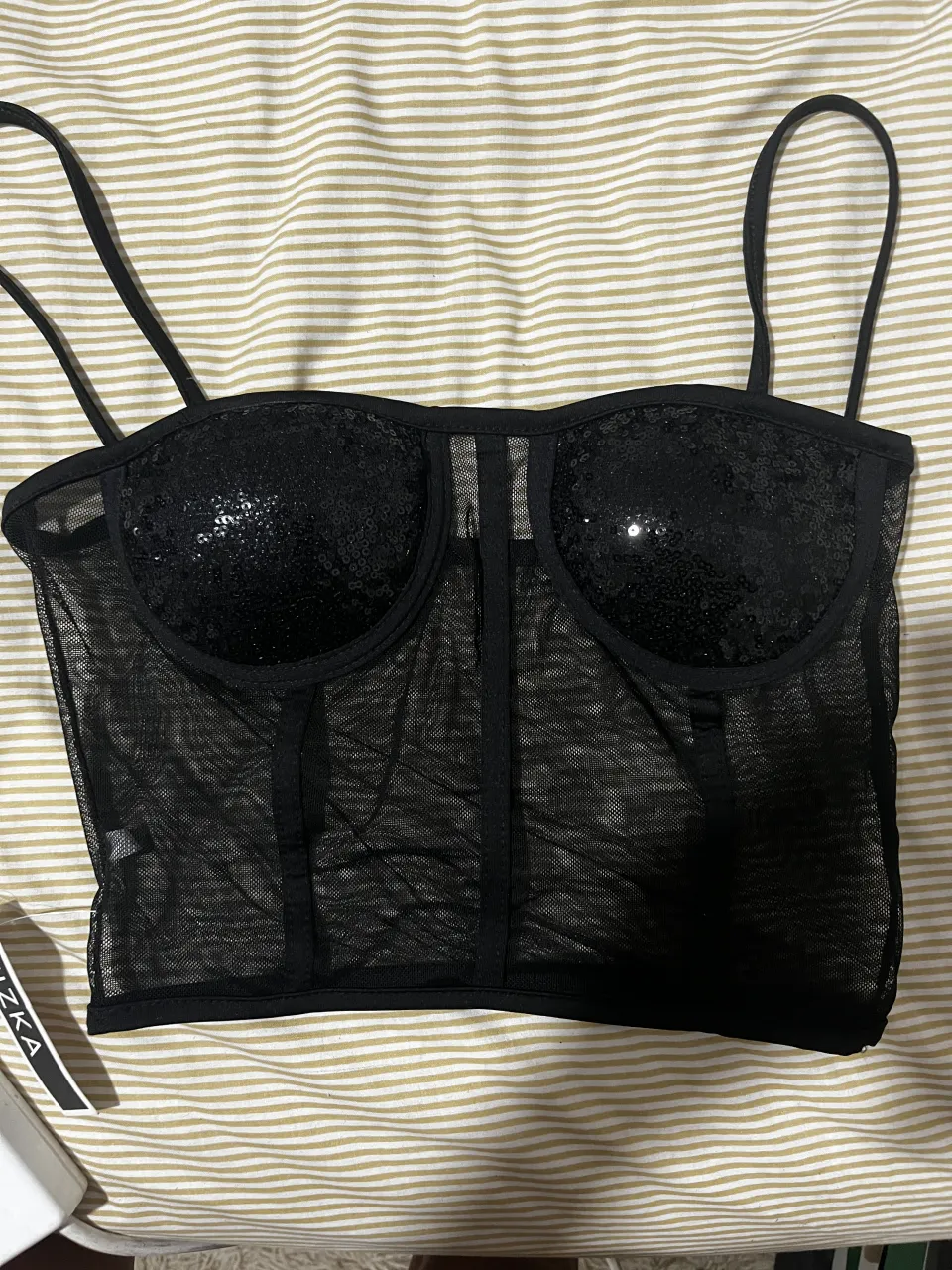 Top negro con lentejuelas en la parte del busto y tiras finas. La parte del abdomen es de tela de red.