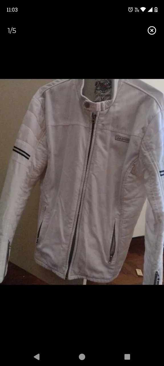 Campera blanca con cierre al frente y bolsillos con cierre. Tiene detalles de franjas negras en las mangas.