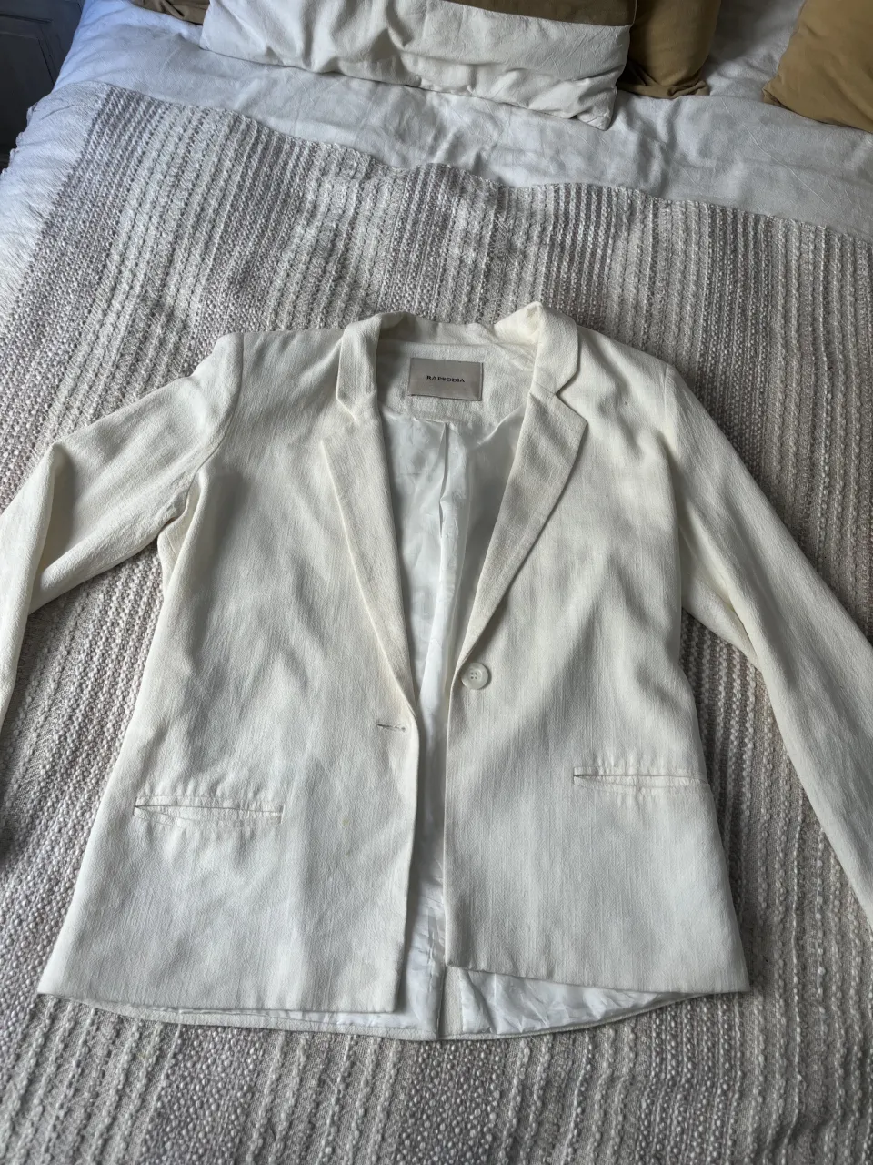 Blazer RAPSODIA blanco de lino con un botón al frente y bolsillos, tiene hombreras sutiles. Talle S/XS