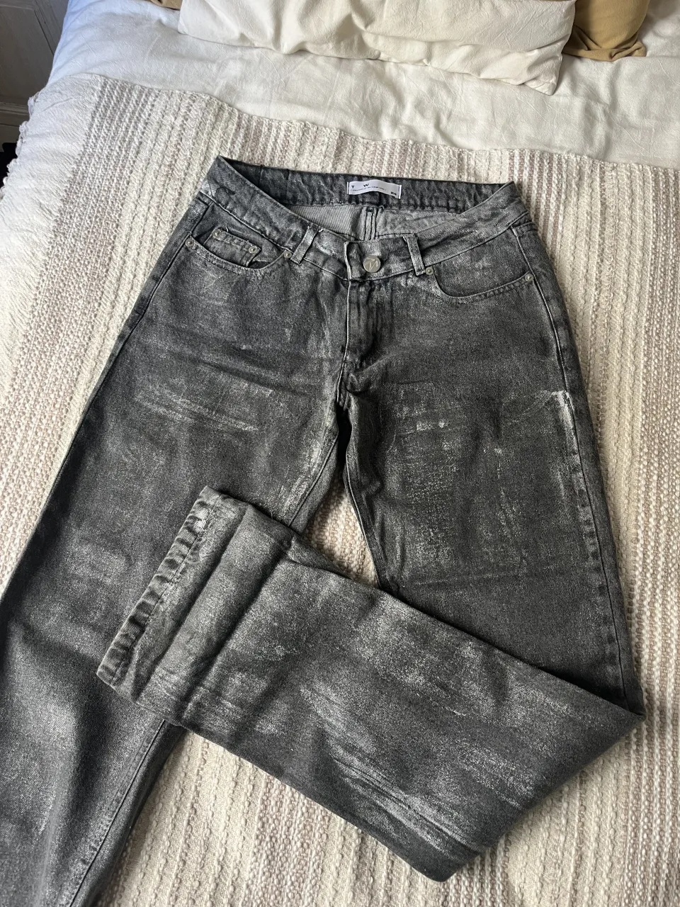 Jeans grises con efecto desgastado y brilloso. Cierre y botón. Tiro bajo/medio 