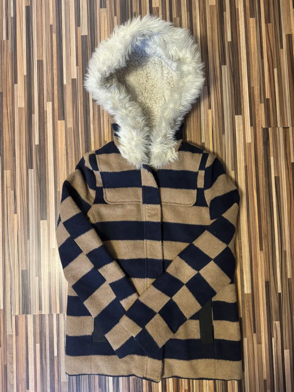 Campera de abrigo para mujer, con diseño a rayas en tonos marrón y azul marino. Posee capucha con borde de piel sintética y forro interior de borrego. Ideal para el invierno.