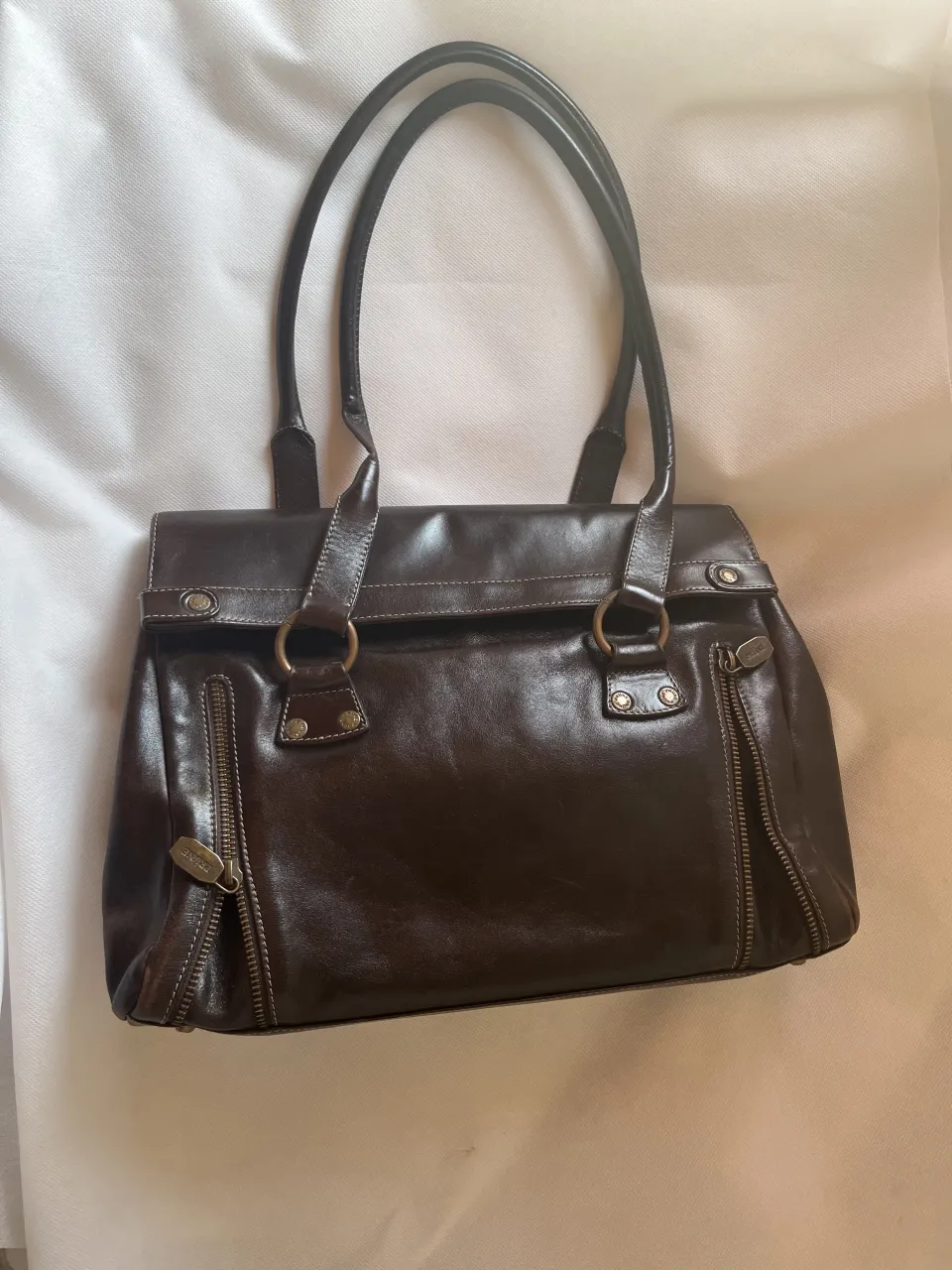 Bolso de cuero marrón oscuro, con detalles de costuras y cierres metálicos. Ideal para el día a día o para complementar un look casual.