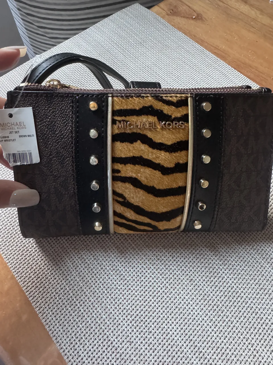Billetera Michael Kors con diseño estampado de animal print y detalles metálicos. Cierre completo y correa de muñeca.