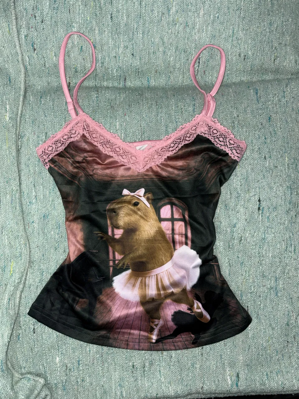 Musculosa con estampa de capibara bailarina de ballet. Posee breteles finos y detalles de encaje rosa en el escote.