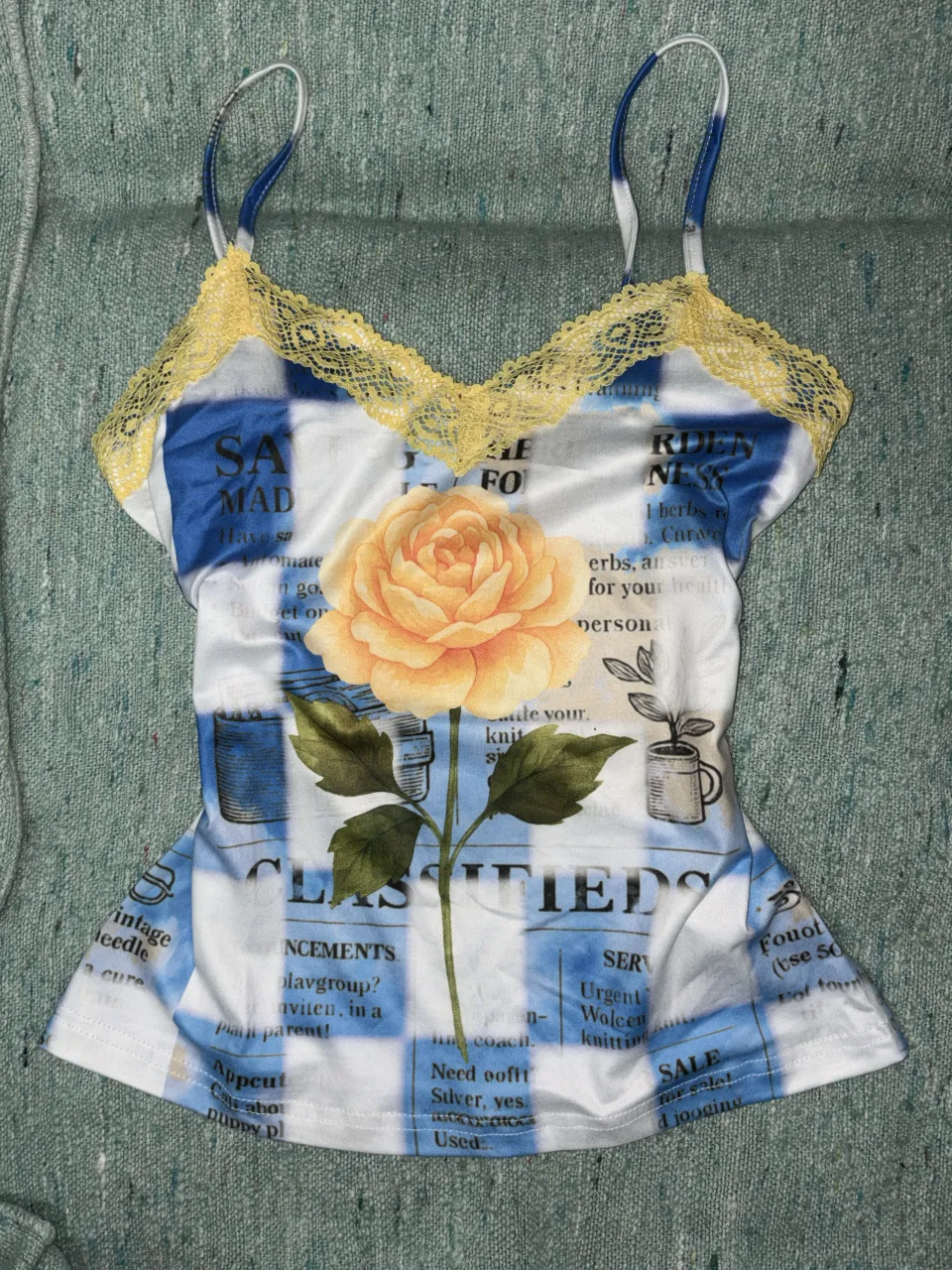 Top con tiras finas y detalles de encaje amarillo en el escote. Estampado de estilo periódico con un gran diseño de rosa amarilla en el centro.