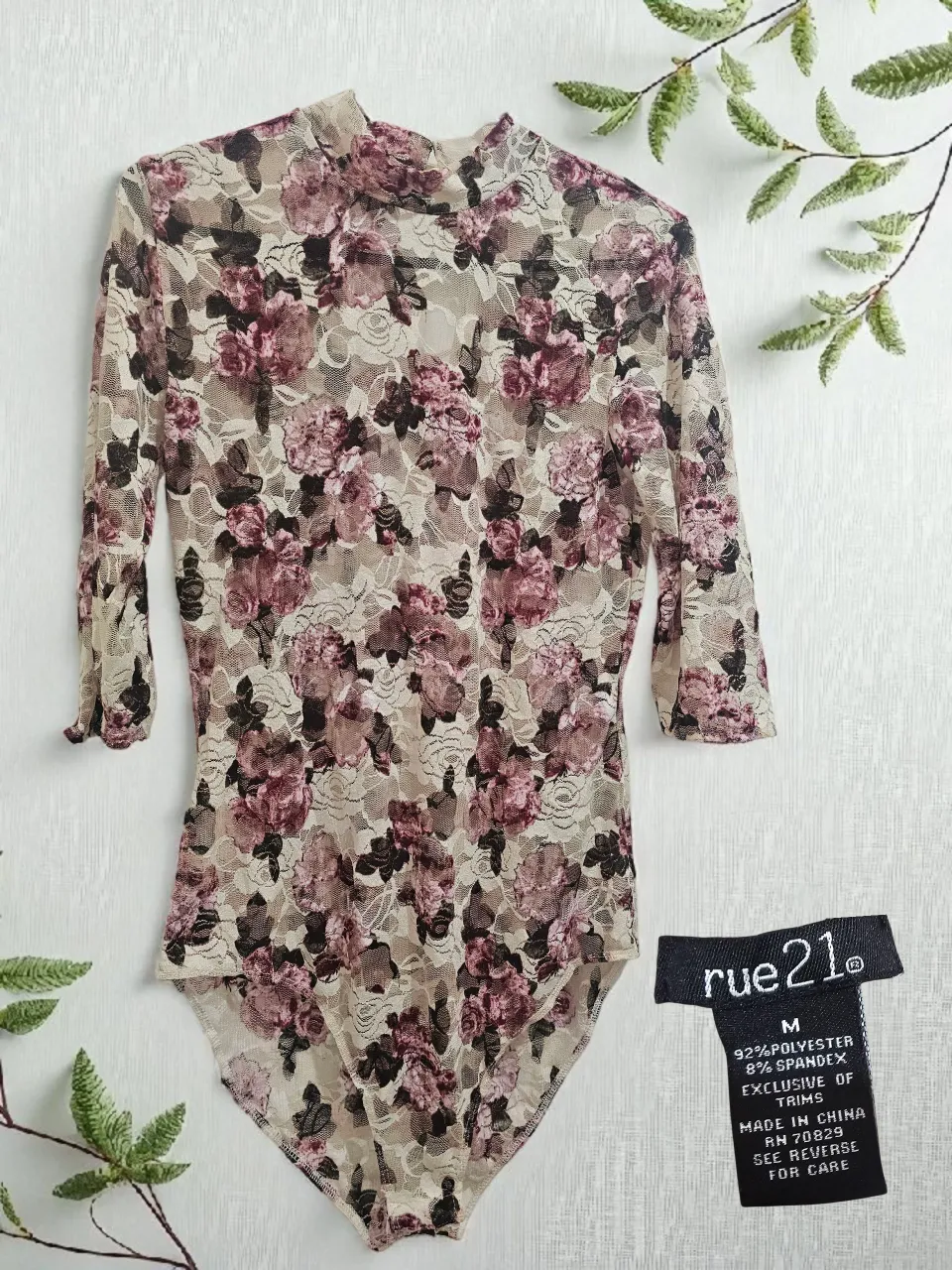 Body de encaje con estampa floral en tonos rosas y beige. Posee cuello alto y mangas 3/4. Ideal para un look romántico y canchero.