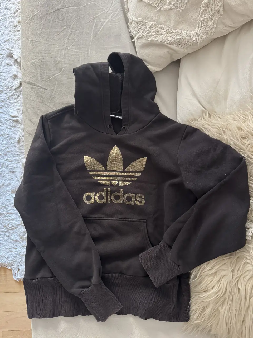 Buzo canguro Adidas negro con logo dorado en el frente. Ideal para un look casual y deportivo.