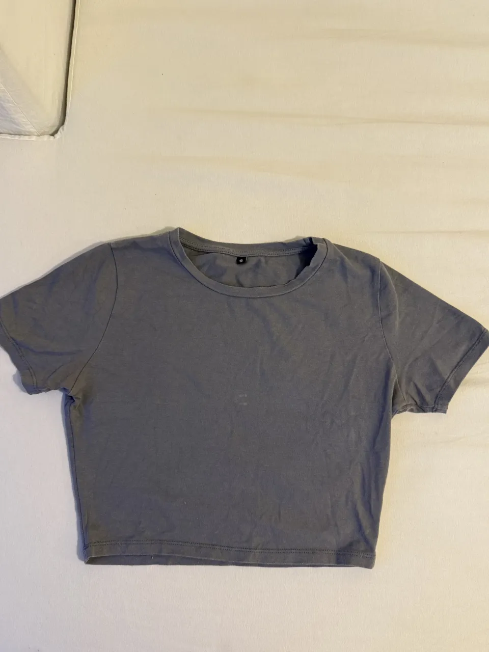 Remera crop gris, manga corta y cuello redondo. Perfecta para un look casual y moderno.